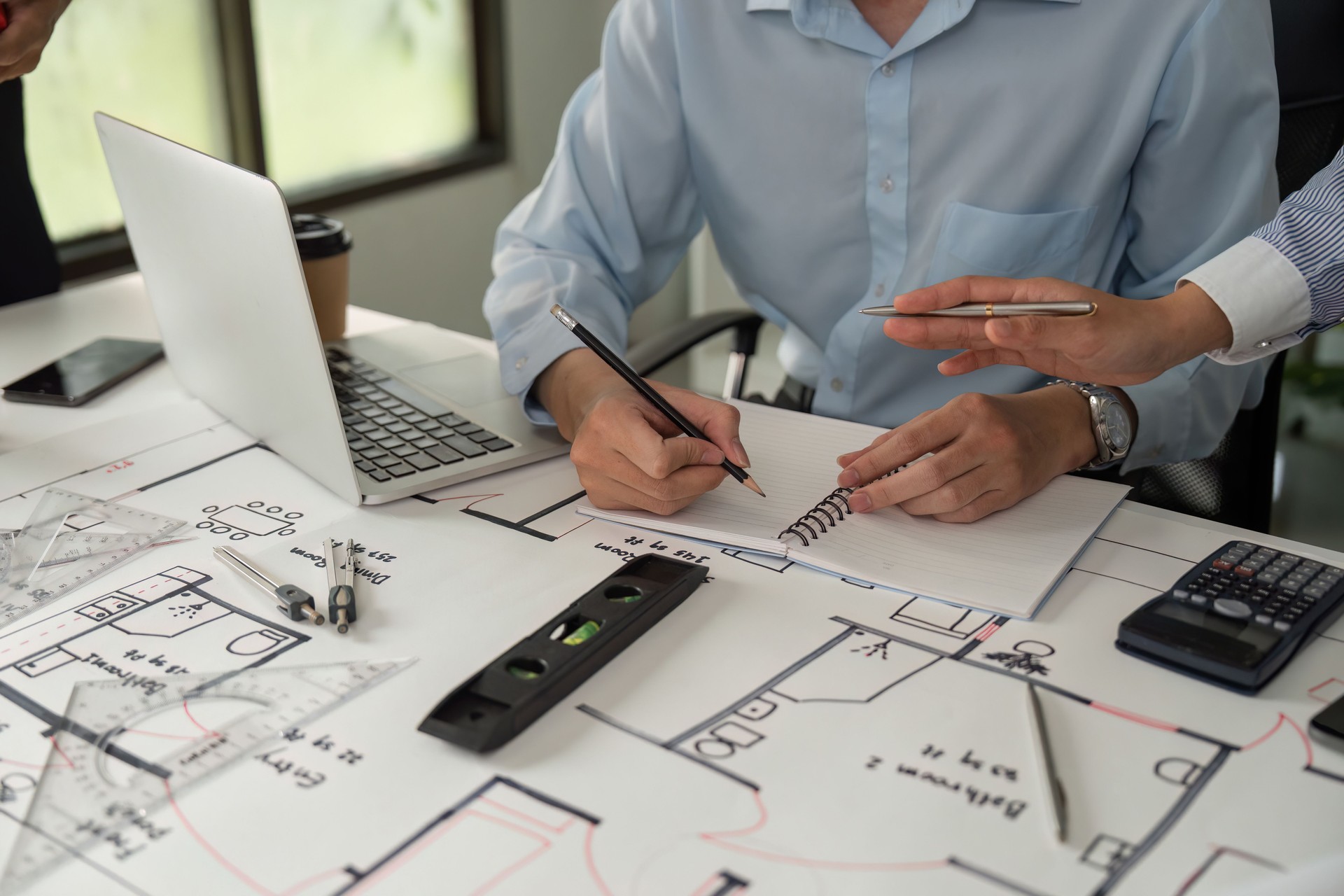 Design and Drafting. An architect taking notes while collaborating on construction plans and specifications.